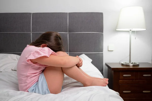 Girl crying in tears sitting on bed in bedroom. Unhappy children feeling sad lonely and upset in dark room at night at home. High quality photo