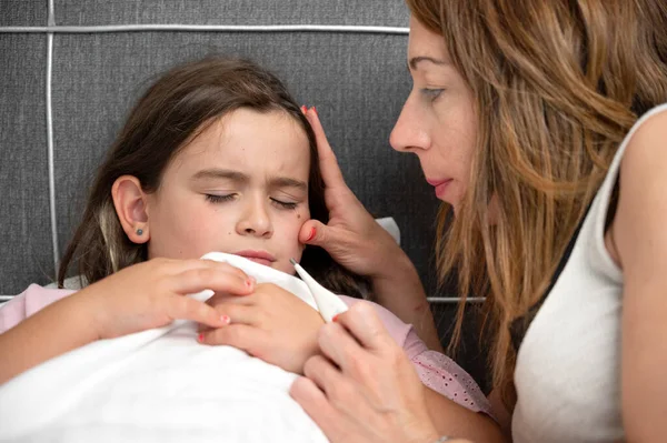 stock image Mother measuring temperature of her ill daughter. Sick child with high fever laying in bed and mother holding thermometer. High quality photo