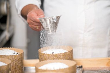 Pasta şefi geleneksel İtalyan panettonlarını pudra şekeriyle süslüyor. Yüksek kaliteli fotoğrafçılık.