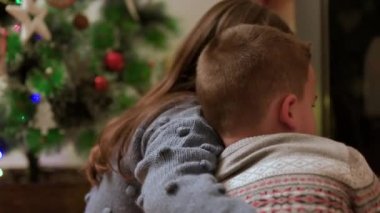 Kardeşler şöminenin önündeki Noel ağacının yanında eğleniyorlar. Aşk, aile ve mutluluk kavramı. Yeni yıl arifesi. Noel zamanı. Işıklı köknar ağacında sıcak bir tatil. Yüksek kalite 4k görüntü