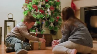 Kardeşler güzel dekore edilmiş Noel ağacıyla oturma odasına koşuyorlar, büyük kutulara sarılmış hediyeleri açmak için sabırsızlanıyorlar. Yüksek kalite 4k görüntü