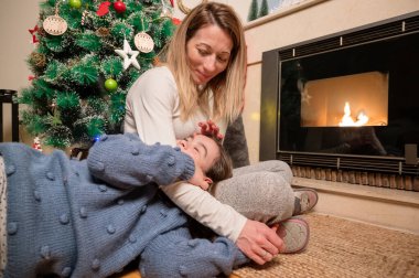 Anne-kız kucaklaşıp gülümsüyor. Kış akşamı, Noel arifesinde dekore edilmiş bir salonda birlikte oturuyorlar. Aile mutluluğu .