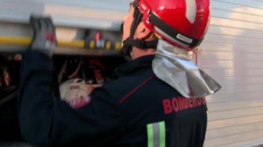 Üniformalı ve koruyucu başlıklı itfaiyeci, depo dolabını açıyor, harekete geçmeye hazırlanıyor. Arka planda itfaiye aracı var. Yüksek kalite 4k görüntü