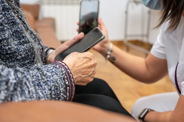 Nurse teaching elder woman how to use mobile phone, senior grandmother learning to use smartphone at nursing home. Modern technology for elderly. High quality photo.
