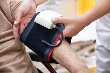 Bakımevindeki yaşlı kadın elinin tansiyonunu ayarlamak için çalışan hemşirenin elini kapat. Yüksek kalite fotoğraf