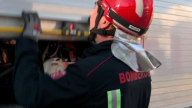 Üniformalı ve koruyucu başlıklı itfaiyeci, depo dolabını açıyor, harekete geçmeye hazırlanıyor. Arka planda itfaiye aracı var. Yüksek kalite 4k görüntü