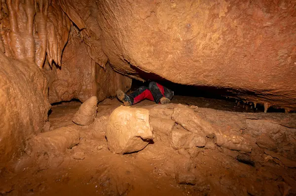 A speleologist with helmet and headlamp exploring a cave with rich stalactite and stalagmite formations. High quality photography.