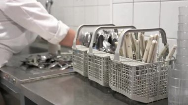 Tanınmayan bir kadın, ticari mutfakta bulaşık makinesinde bulaşık yıkamak için kirli çatal bıçak takımı hazırlıyor. Yüksek kalite 4k görüntü