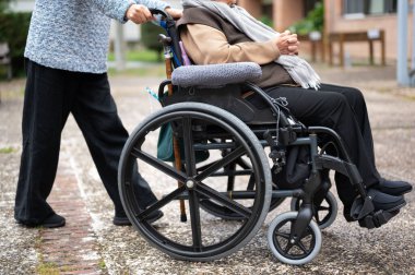 Tekerlekli sandalyedeki yaşlı kadın kızıyla huzurevinin bahçesinde vakit geçiriyor. Yüksek kaliteli fotoğrafçılık