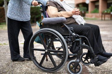 Tekerlekli sandalyedeki yaşlı kadın kızıyla huzurevinin bahçesinde vakit geçiriyor. Yüksek kaliteli fotoğrafçılık