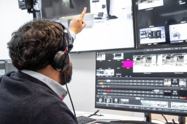 Yayın kontrol odasında canlı bir prodüksiyona rehberlik eden bir televizyon yönetmeni. Birden fazla ekranla çevrili yönetmen, bir kulaklık takar ve bir video değiştiriciye doğru hareket eder..