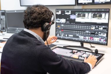 Yayın kontrol odasında canlı bir prodüksiyona rehberlik eden bir televizyon yönetmeni. Birden fazla ekranla çevrili yönetmen, bir kulaklık takar ve bir video değiştiriciye doğru hareket eder..