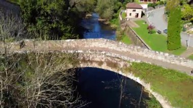 İspanya, Cantabria 'da tarihi bir köy olan Lierganes' in insansız hava aracı görüntüsü. Sahnede geleneksel taş evler, kırmızı kiremitli çatılar, Miera Nehri üzerindeki ortaçağ köprüsü ve kasabayı çevreleyen yemyeşil tepeler yer alıyor. Yüksek kalite 4k görüntü