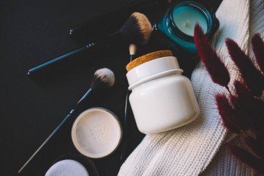 Siyah arka planda kozmetik, mum, fırça ve çiçekler