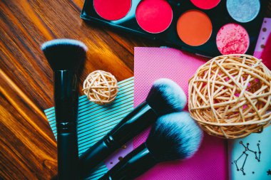 Göz farı paleti ile makyaj fırçaları ve ahşap arka planda bir not defteri..