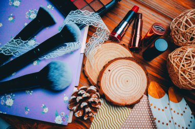 Göz falı paleti, ruj, makyaj fırçası ve kahverengi ahşap arka planda not defteri.