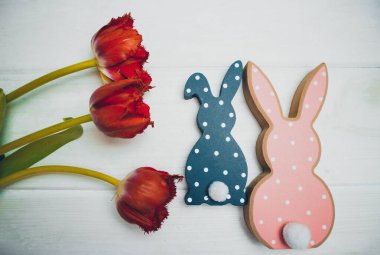 Tavşanlar, yumurtalar, beyaz ahşap arka planda kırmızı laleler.