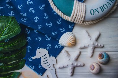 Yaşam şamandırası, denizyıldızı, denizatı, kabuklar, yeşil yapraklar ve ahşap beyaz arka planda kumaşa sabitlenmiş çapa. Yaz mevsimi