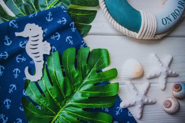 Yaşam şamandırası, denizyıldızı, denizatı, kabuklar, yeşil yapraklar ve ahşap beyaz arka planda kumaşa sabitlenmiş çapa. Yaz mevsimi