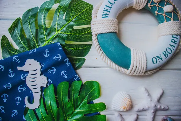 Yaşam şamandırası, denizyıldızı, denizatı, kabuklar, yeşil yapraklar ve ahşap beyaz arka planda kumaşa sabitlenmiş çapa. Yaz mevsimi