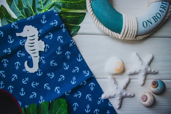 Yaşam şamandırası, denizyıldızı, denizatı, kabuklar, yeşil yapraklar ve ahşap beyaz arka planda kumaşa sabitlenmiş çapa. Yaz mevsimi