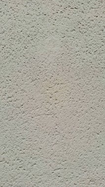 Işıklı, nötr renkte desenli bir duvar yüzeyi. Yüzey pürüzlü ve gözenekli görünüyor, küçük çıkıntıların ve girintilerin ince bir kalıbını gösteriyor..