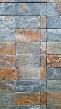 Gri ve turuncunun çeşitli tonlarında dikdörtgen taş fayanslardan yapılmış, doğal desenler ve renkler gösteren dokulu bir duvar..