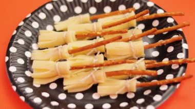 Cadılar Bayramı partisi için yenilebilir cadı süpürgeleri. Manchego peyniri ve krakerle yapılıyor. Lezzetli çerez. Turuncu arka plan. Dekoratif tek kullanımlık tabak.