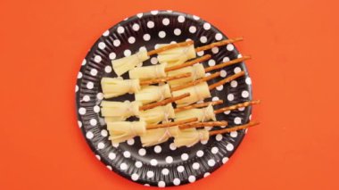 Cadılar Bayramı partisi için yenilebilir cadı süpürgeleri. Manchego peyniri ve krakerle yapılıyor. Lezzetli çerez. Turuncu arka plan. Dekoratif tek kullanımlık tabak. Tam çekim.