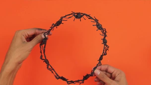 黒のプラスチッククモで作られた頭冠 ハロウィンパーティーのための怖い工芸品や工芸品 オレンジの背景 茶色の手 — ストック動画
