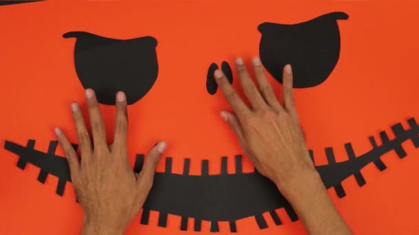 暗い工芸品 オレンジの背景に黒いハロウィンの顔 茶色い肌の手 — ストック動画