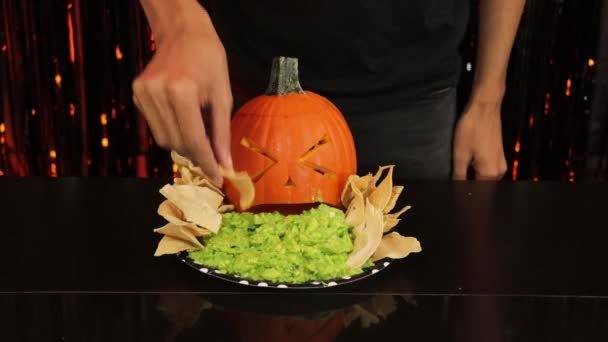 怖いカボチャのスパイグアカモーレを作る ハロウィンパーティーのための食べ物 皿の上にナチョスが乗っていておいしそうです — ストック動画