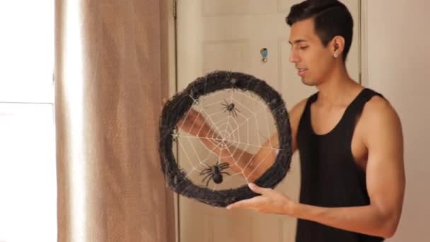 彼の家を飾るために不気味なハロウィーンの花輪をぶら下げている若いラテン人 — ストック動画