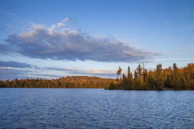 Kuzey Minnesota 'da günbatımında sonbahar renklerinde ağaçlar ve tepelerle mavi alabalık gölü