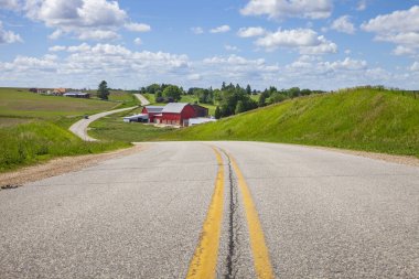 Iowa kırsalında, parlak bir bahar gününde kavisli bir yolda kırmızı bir ahırı olan bir çiftlik.
