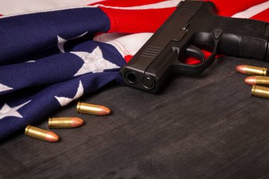 Kurşunlu tabanca ve siyah arka planda Amerikan bayrağı.