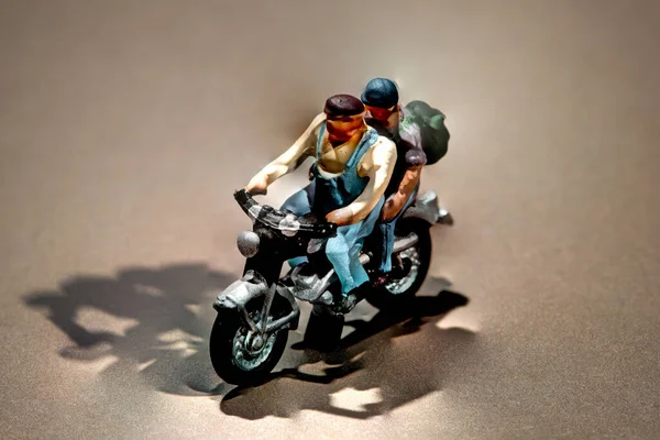 バックパックを身に着けているミニチュア男性コピースペースと影を持つ茶色の背景にバイクで旅行に行く — ストック写真