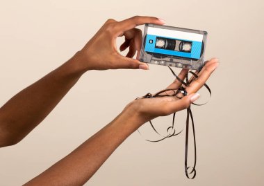 Siyahi kadının elleri bej arka planda bant ile kaset gösteriyor.