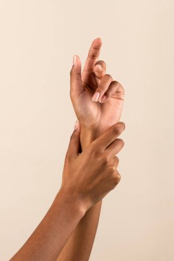 Hands of African American female touching wrist and demonstrating perfect manicure against beige background
