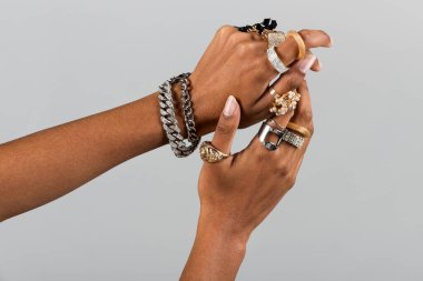 Crop anonymous African American female hands with bracelet and different gold and silver rings on gray background