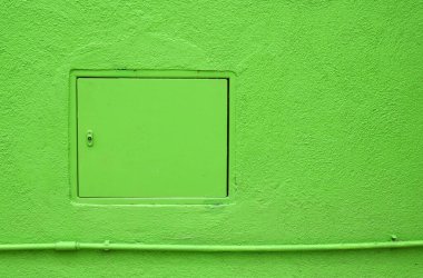 Closed inspection hatch located over pipe on plaster wall of bright green building