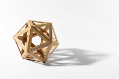 Platonic solid icosahedron shape made of light wood casting shadow on gray background
