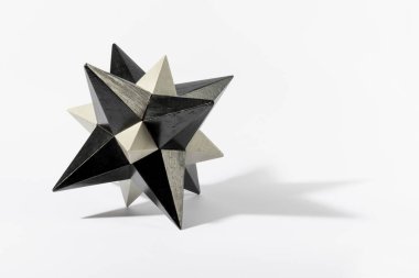 Lumber stellated dodecahedron of gray color with pointed ends casting shadow against white background