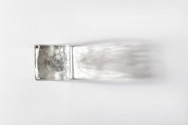 Beyaz arkaplanda gölgesi olan şeffaf parlayan buz küpünün üst görünümü