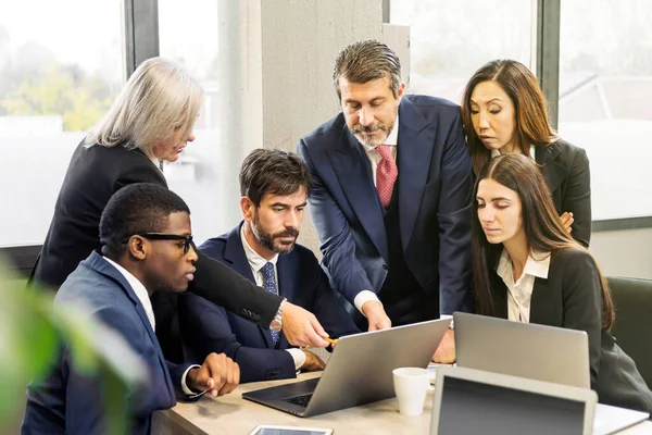 Group of multiracial businesspeople pointing at laptop screen and discussing data during work in office