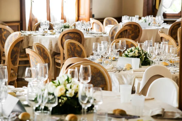 ライトレストランで結婚式のお祝いのために用意されたカトラリーやナプキン付きのワイングラスとホワイトプレート付きのテーブルを提供します — ストック写真