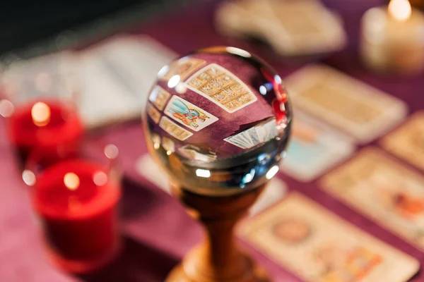 玻璃水晶球在塔罗牌附近的选择性聚焦及在模糊背景下燃点蜡烛预测未来 免版税图库照片