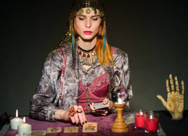 Yetişkin bir kadın falcı. Masada elinde mumlar ve sihirli kristal küre konseptiyle oturmuş tarot kartları okuyor. Kehanet astrolojisi ve ezoterizmi.