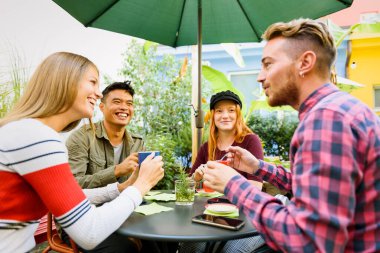 Dışarıdaki kafede kahve molası sırasında masada otururken gülen ve birbirleriyle konuşan çok ırklı kadın ve erkekler.