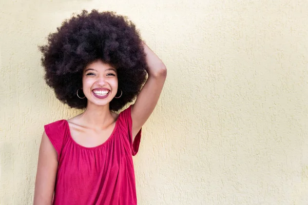 미소와 베이지색 배경에 카메라를 아프로 스타일 긍정적인 아프리카계 여성의 초상화 — 스톡 사진
